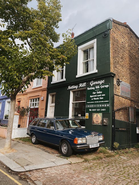 Image of a vintage blue station wagon parked outside a green-painted, two-story commercial building with white-framed windows and a sign that reads 'Nothing Hill Garage' on the front. The building's f